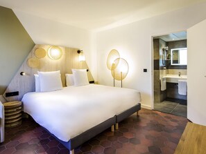 A modern hotel room with a large bed, a wooden headboard, a bedside table, and a bathroom visible through an open door.