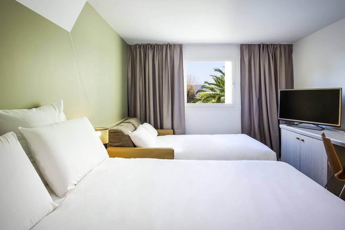 A hotel room with two beds, a TV, and a window with curtains.