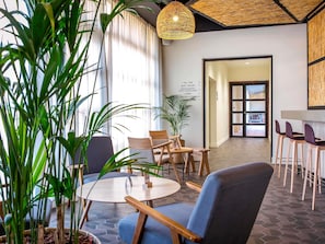 A modern interior with a round table, chairs, potted plants, and a hanging light fixture. - Mercure Cannes Mandelieu (Mandelieu-La-Napoule)