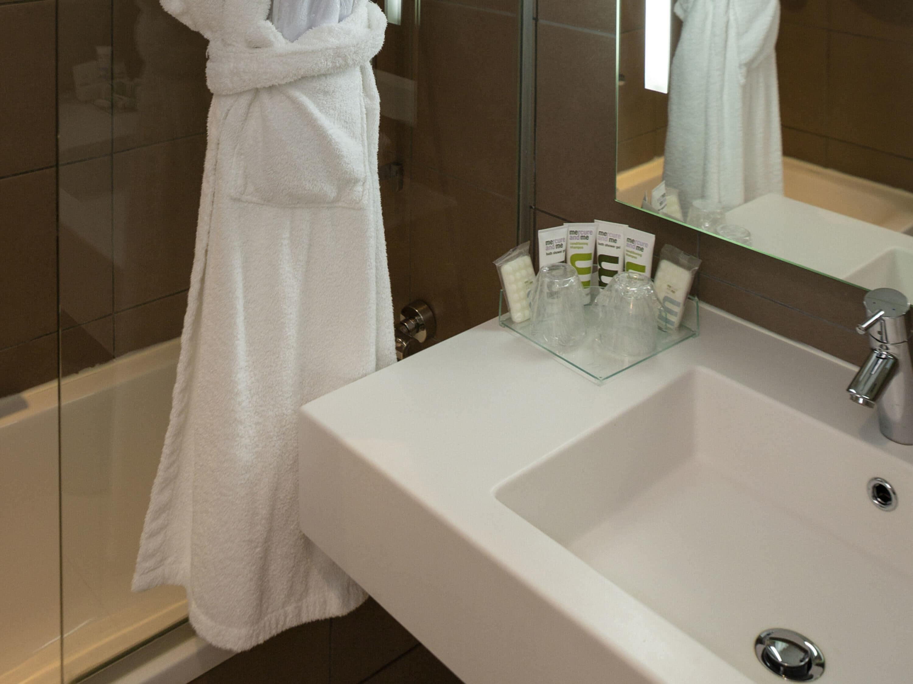 A bathroom with a white sink, a glass shower enclosure, and a white bathrobe hanging on a towel rack.