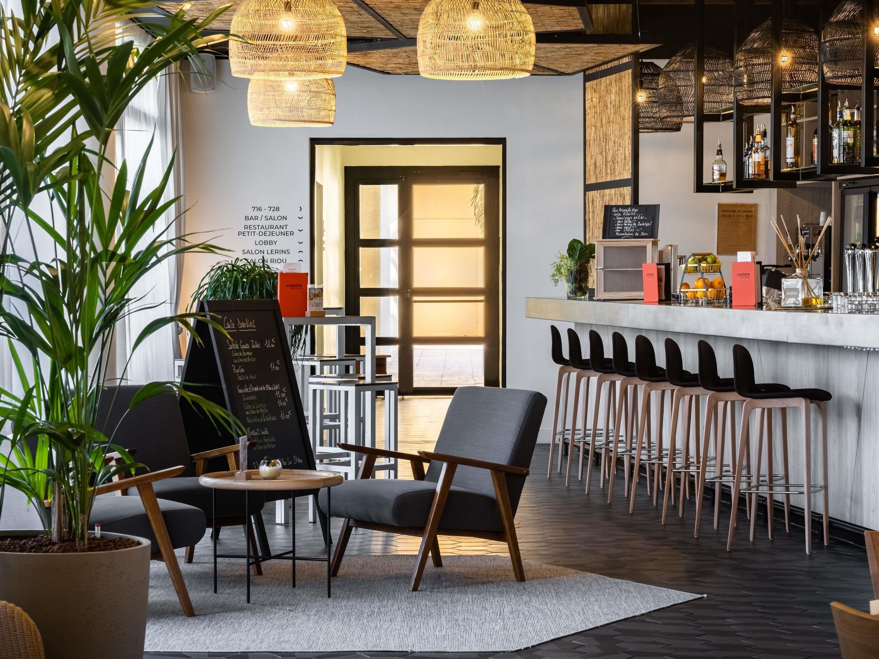 Zona de bar moderna con un menú en pizarra, sillas de madera y una barra con botellas.
