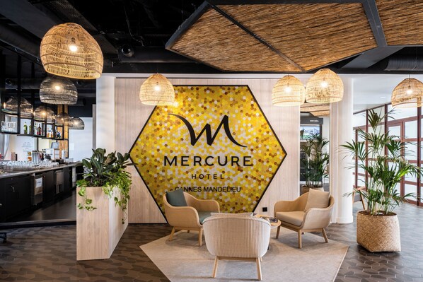 Un vestíbulo con mobiliario de mimbre, un letrero hexagonal grande y plantas en macetas.