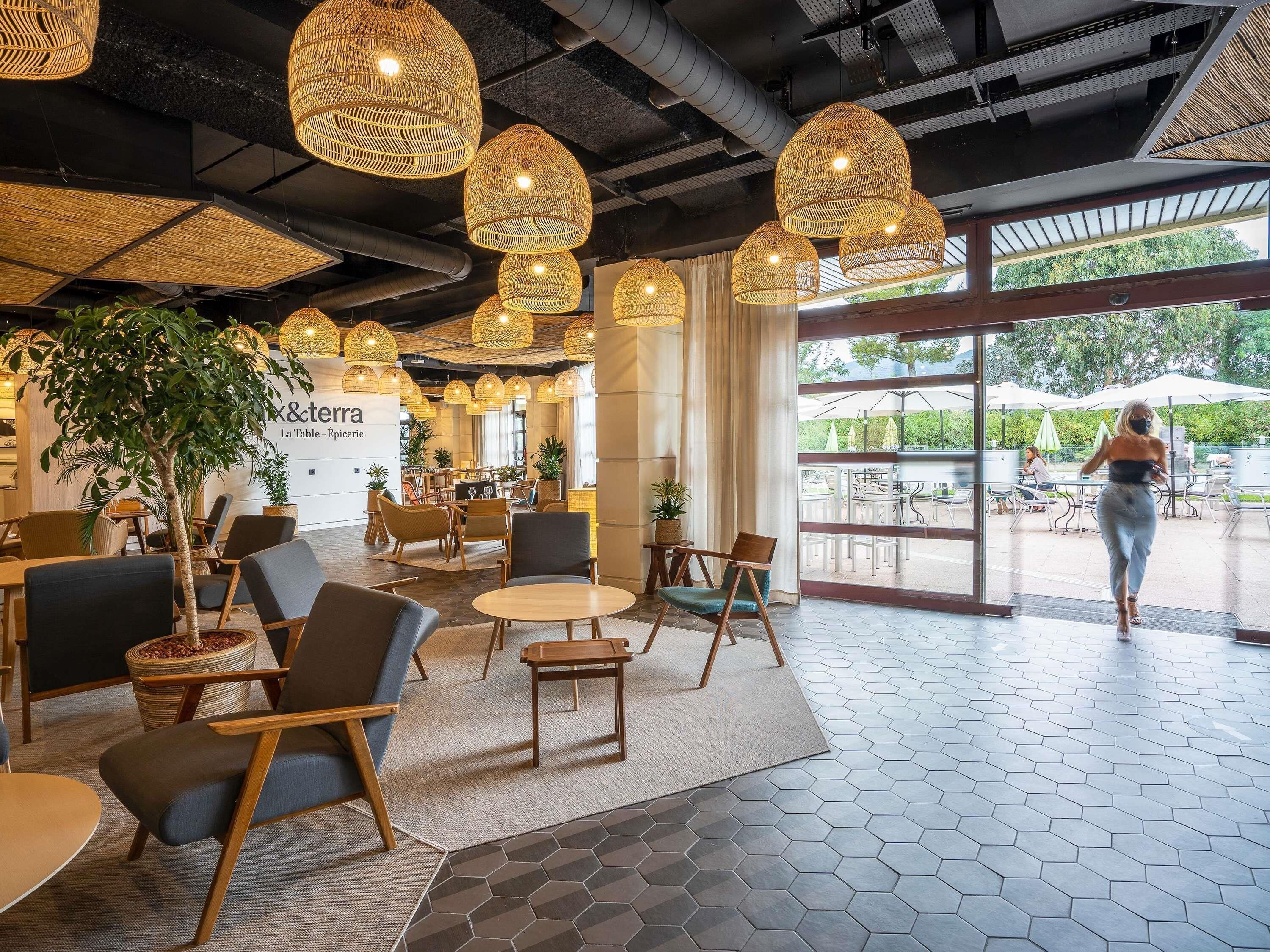 Um café moderno com luminárias pendentes de vime, mobiliário de madeira e vista para o exterior.