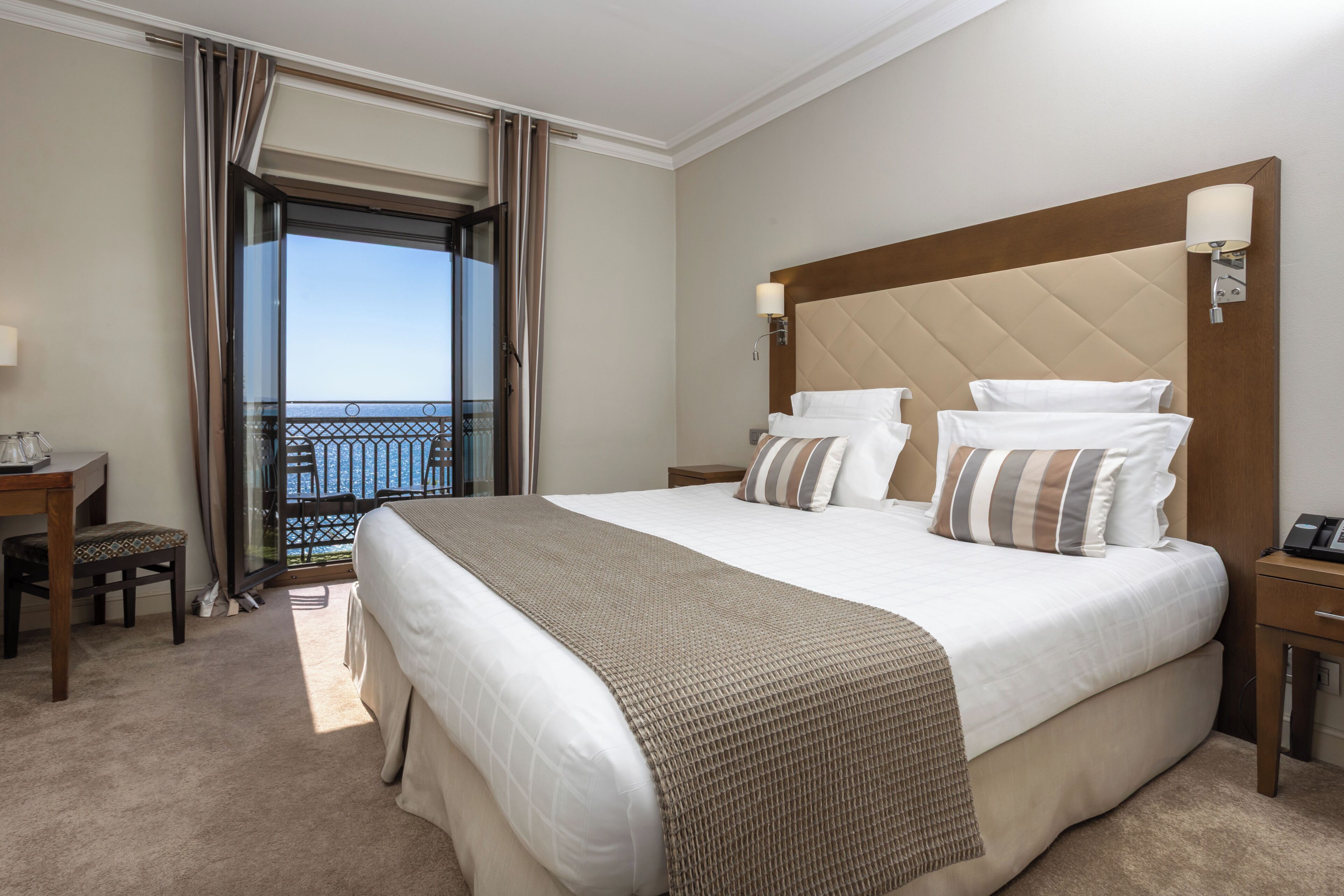 A hotel room with a large bed, a desk, a chair, and a balcony with a view.