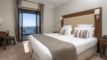 A hotel room with a large bed, a desk, a chair, and a balcony with a view.