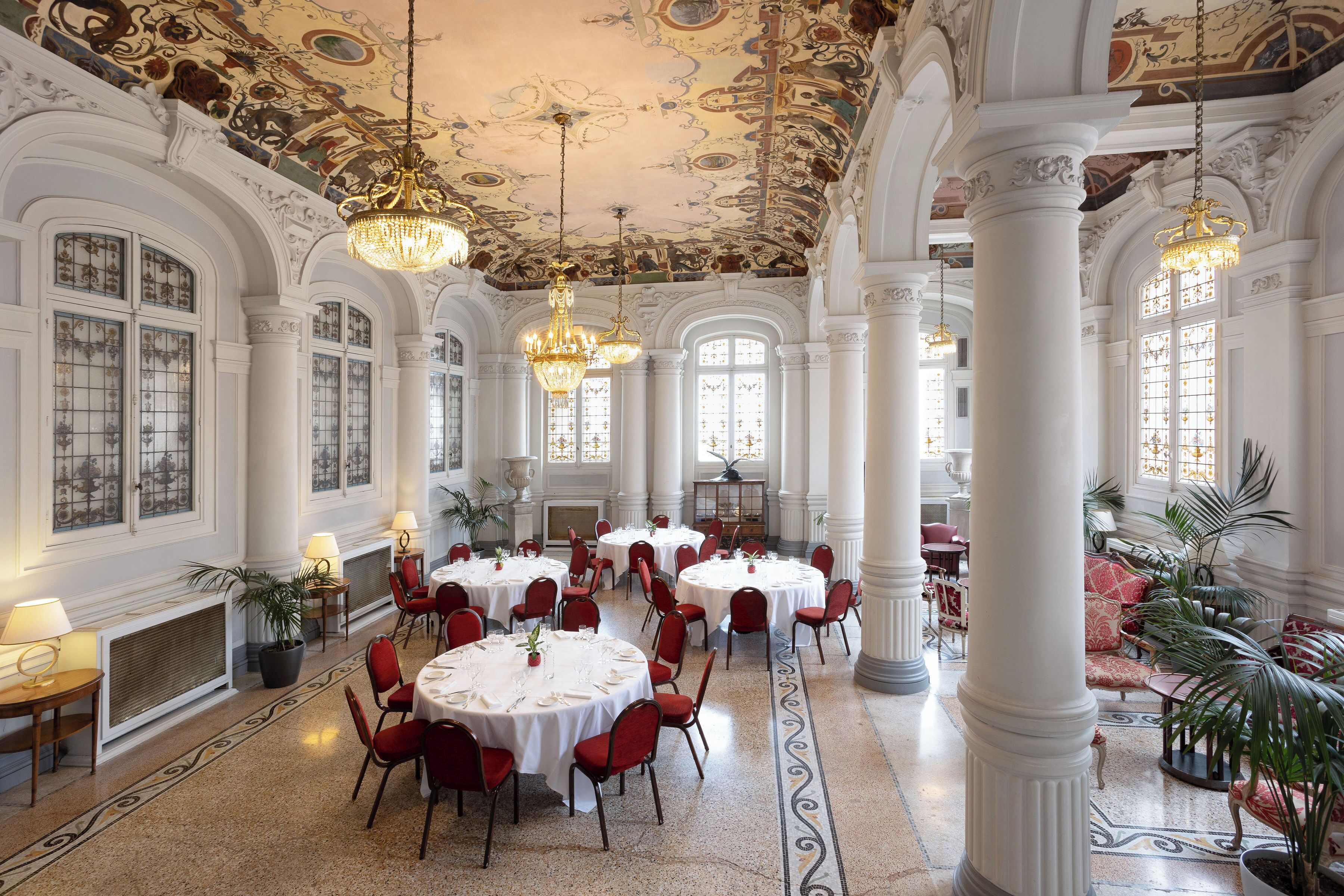 A grand hall with ornate ceiling, large windows, and elegant chandeliers.
