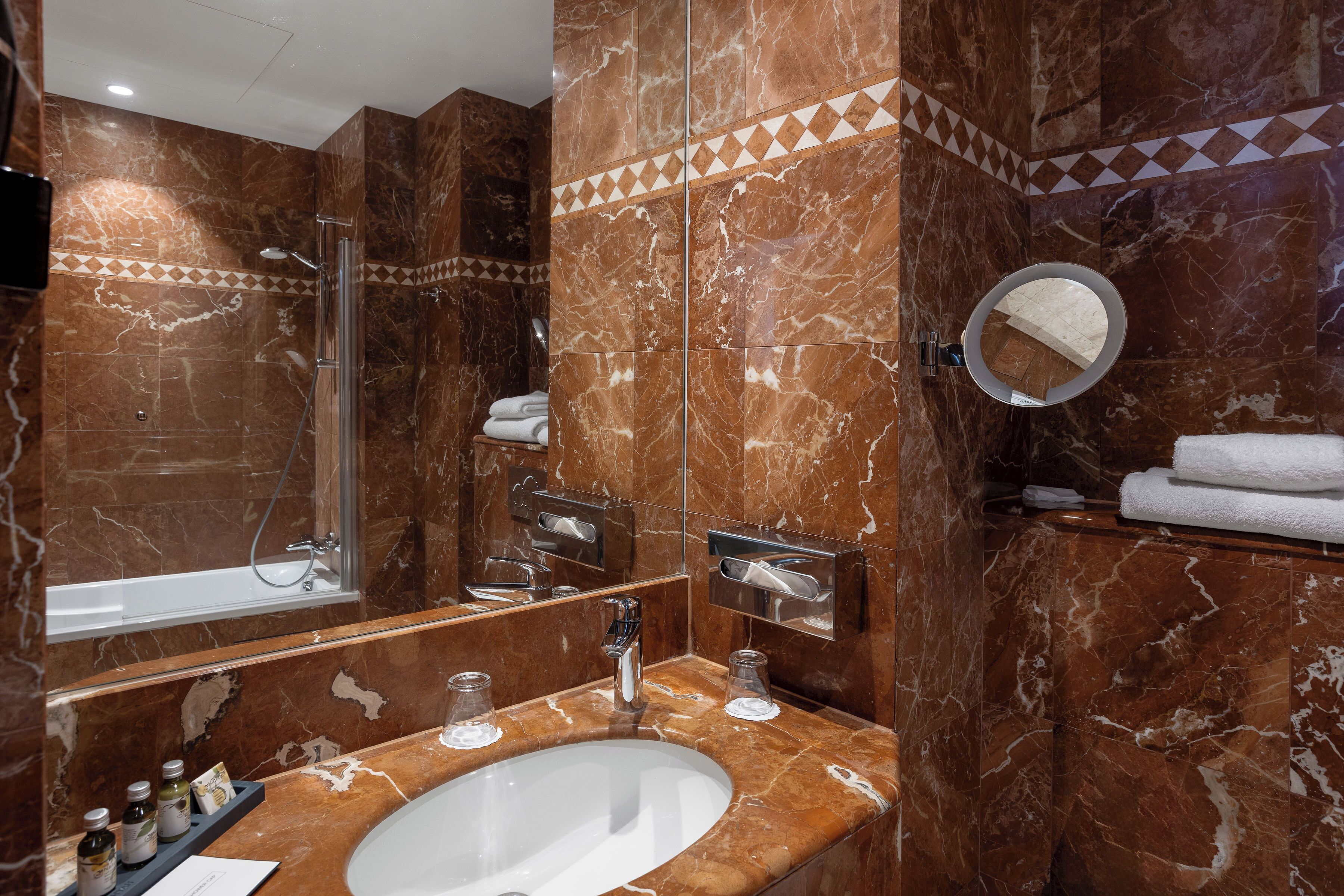 Un baño con lavamanos de mármol, cabina de ducha de vidrio, espejo y toallero.