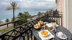 A balcony with a table set for breakfast overlooking a coastal view.