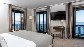 Habitación de hotel con cama, escritorio, silla, televisor y balcón con vista al mar.