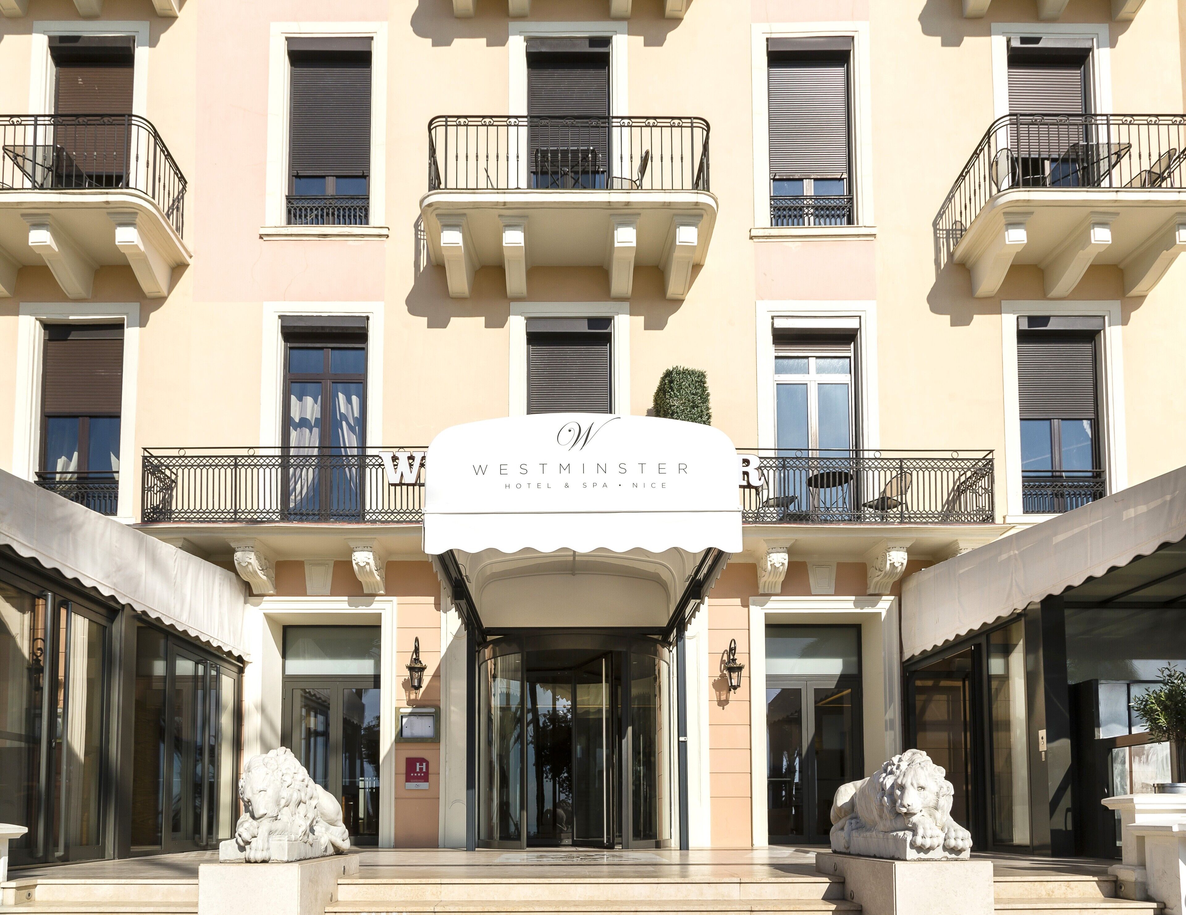 La entrada de un hotel con un letrero que dice 'WESTMINSTER HOTEL & SPA', presenta una fachada clásica, varios balcones y una estatua de león en la entrada.
