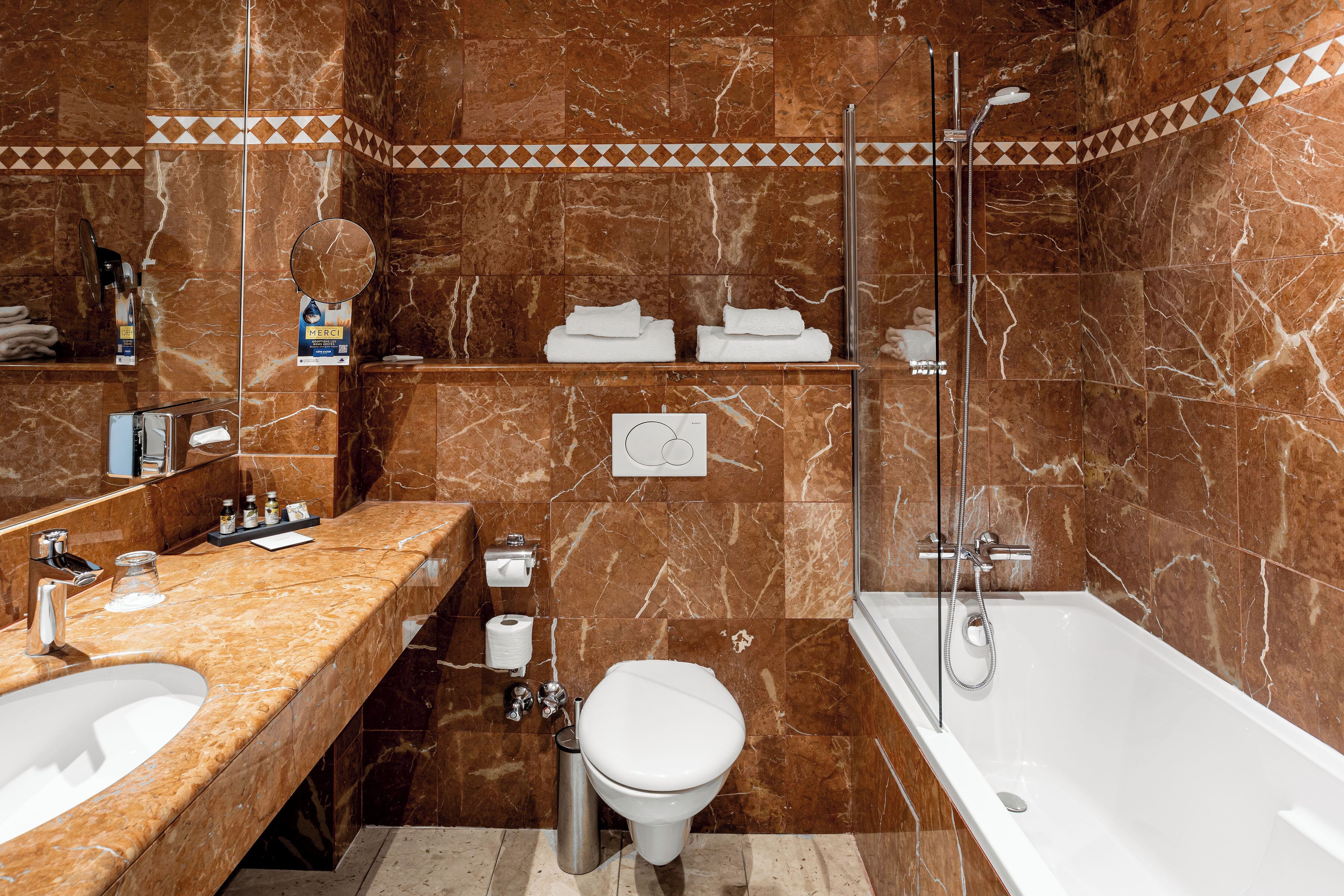 Une salle de bain avec des murs en marbre, une baignoire, des toilettes et un lavabo.