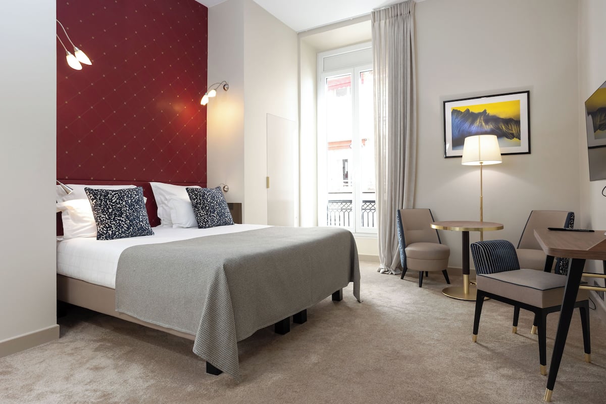 Hotellihuone, jossa on sänky, työpöytä, tuoli, lamppu ja taulu seinällä.