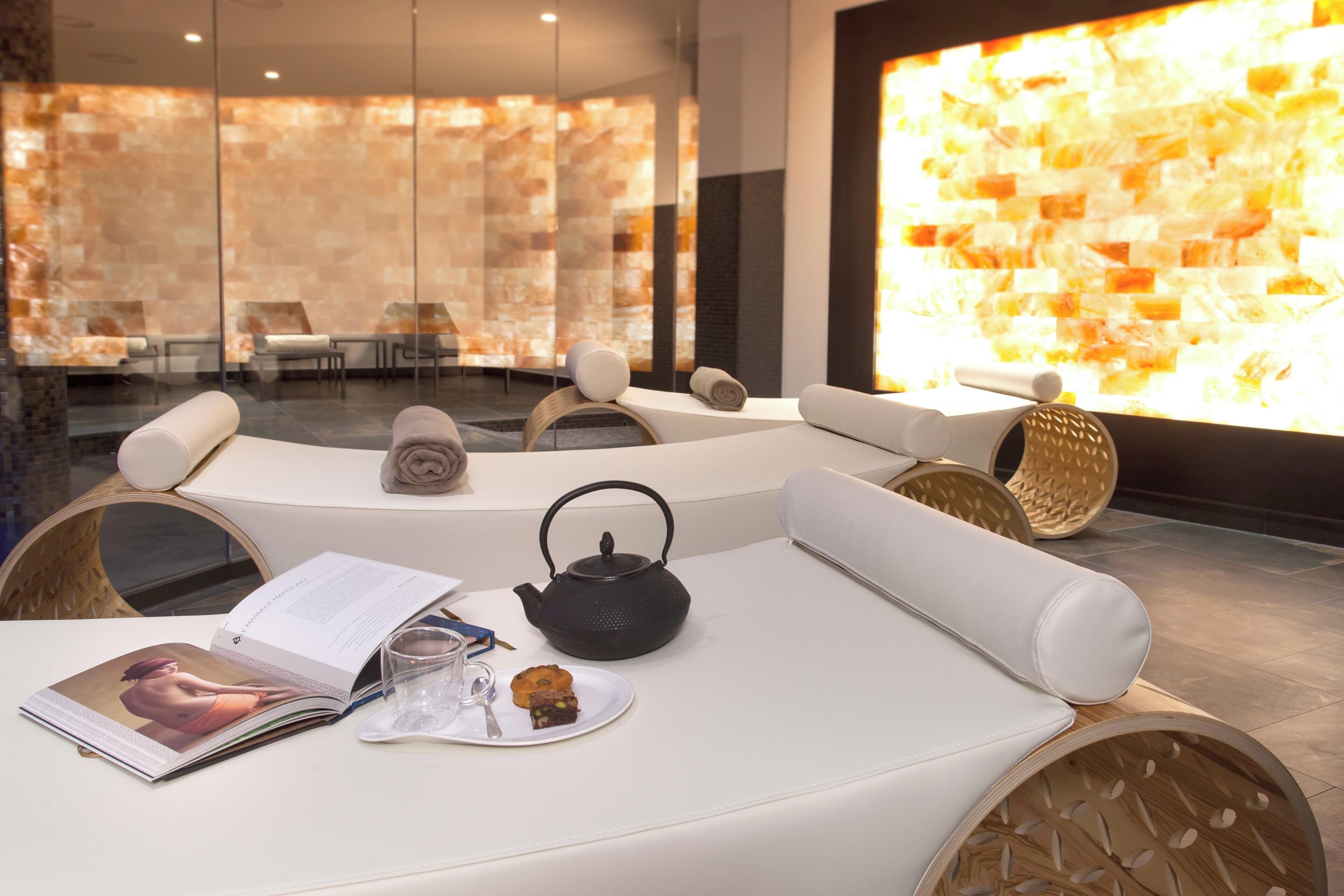 A modern spa room with a white sofa, a tea kettle, a magazine, and a plate with a cookie.