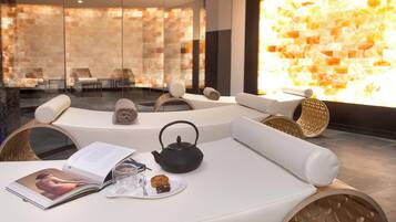 A modern spa room with a white sofa, a tea kettle, a magazine, and a plate with a cookie.
