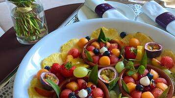 A dining table with a white plate of fruit salad and a vase of flowers.