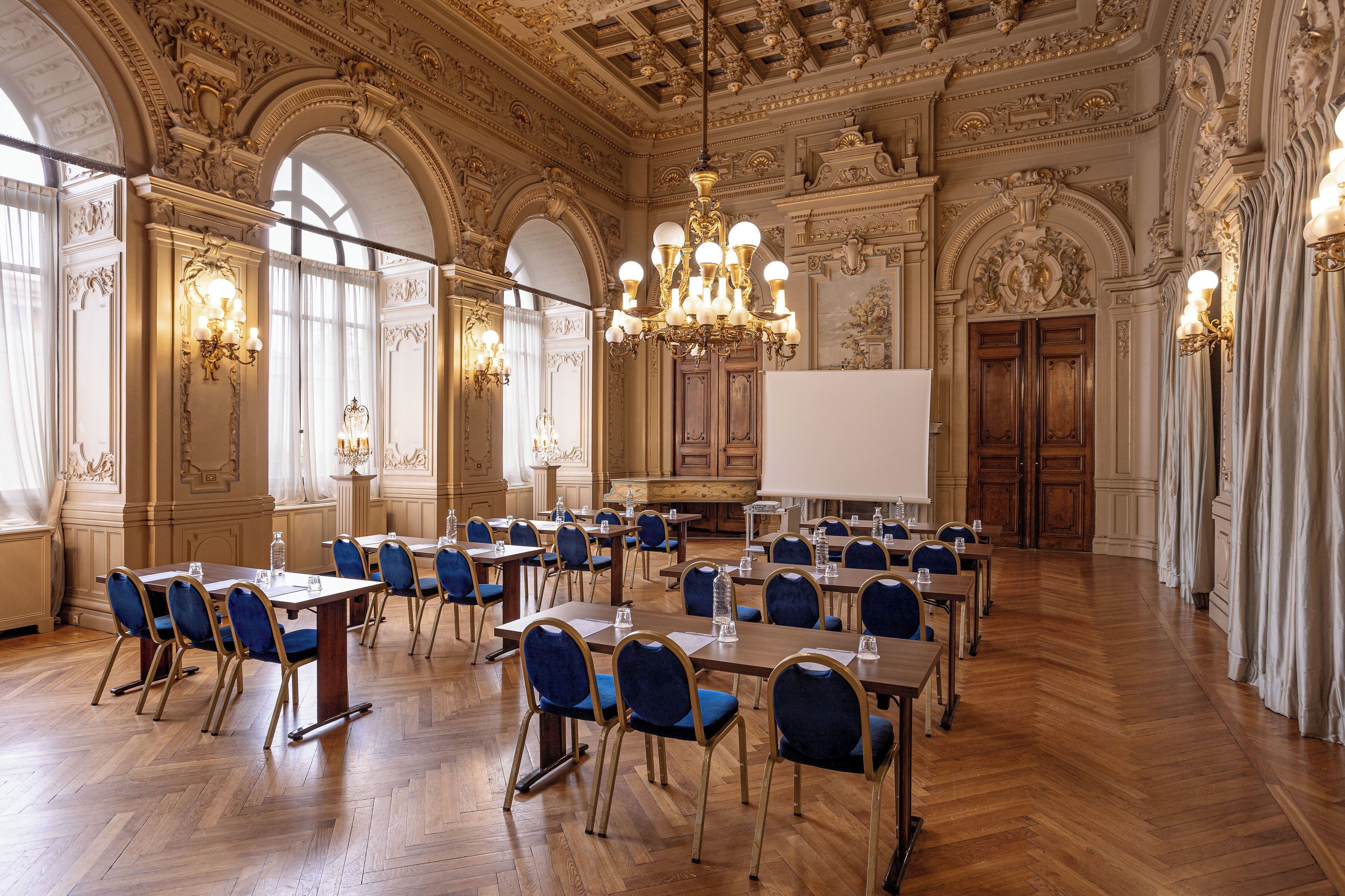 Un vaste hall doté d’un plafond richement décoré, de lustres et d’un tableau blanc à l’avant.