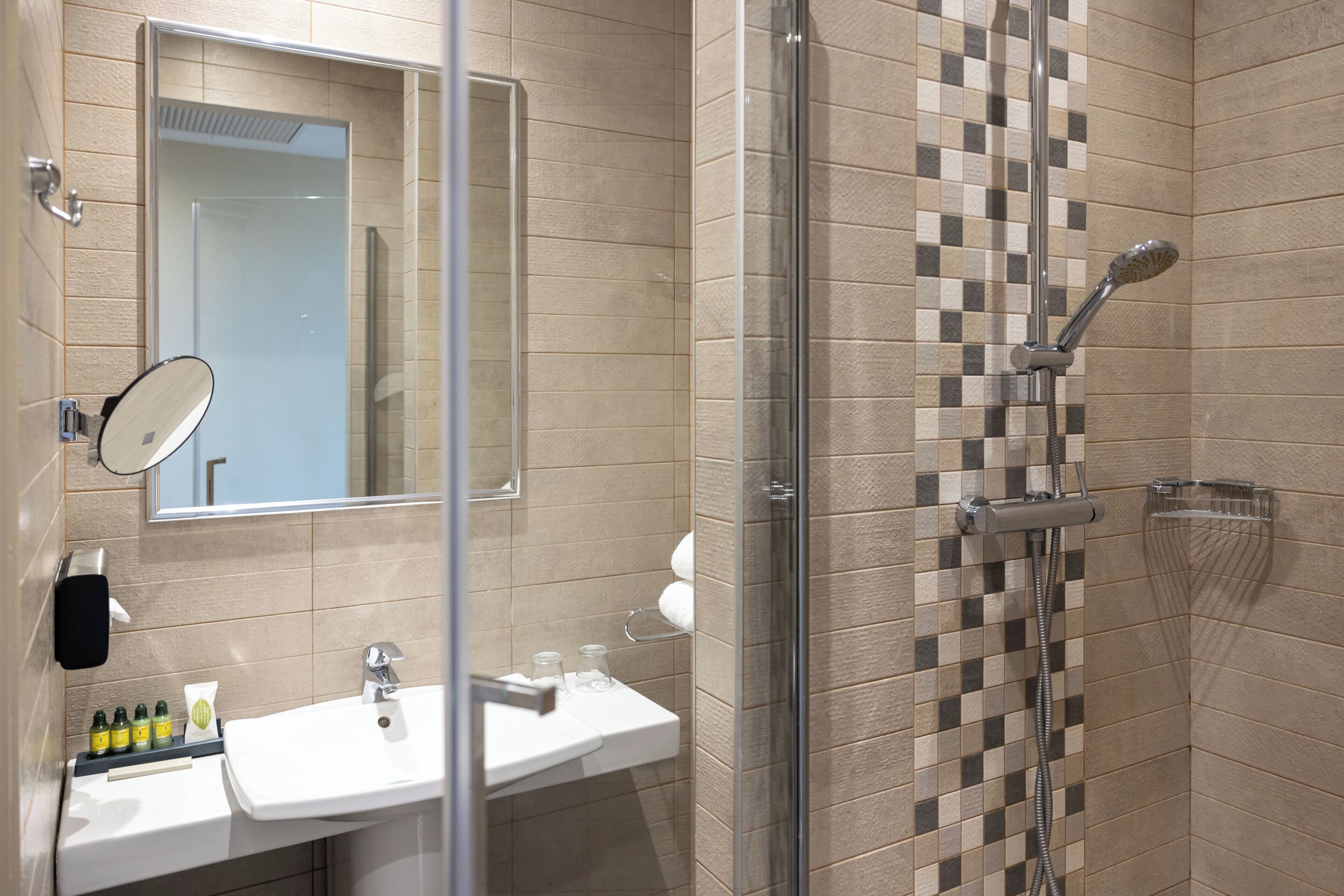 A bathroom with a glass-enclosed shower, a sink with toiletries, and a mirror.