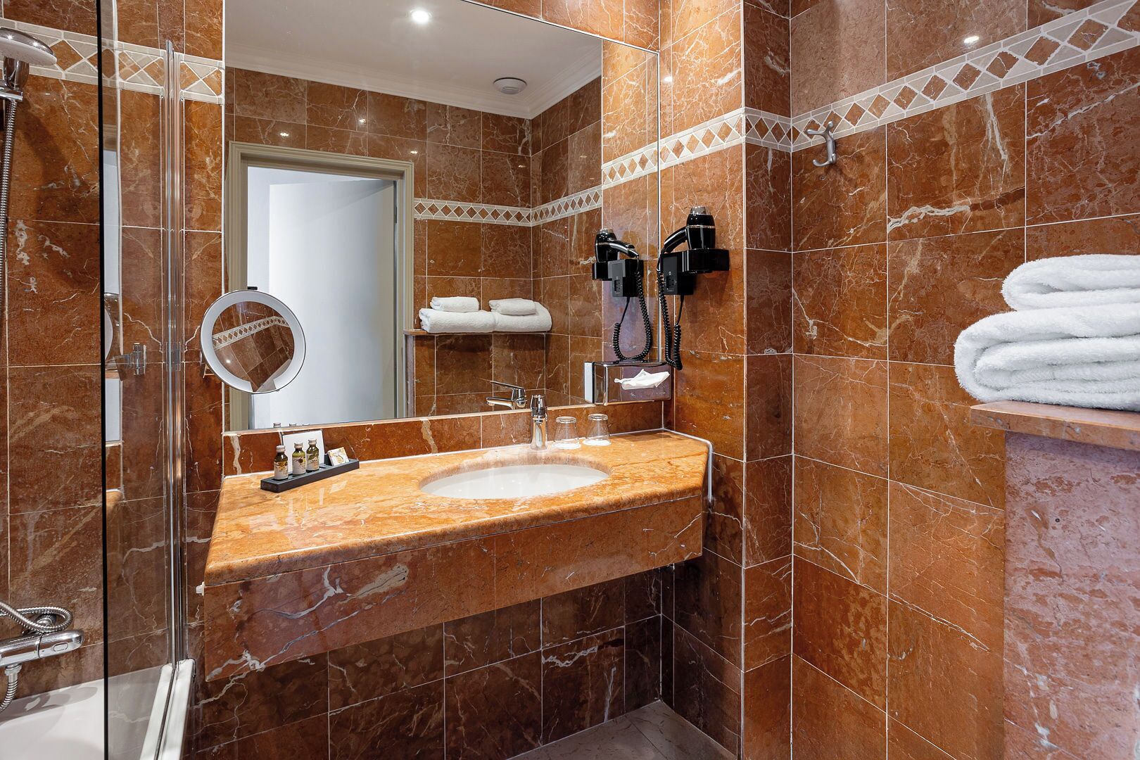 A bathroom with a marble sink, a glass shower enclosure, and a towel rack with folded towels.