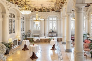 Un amplio vestíbulo con columnas ornamentadas, candelabros y un suelo de mármol pulido.