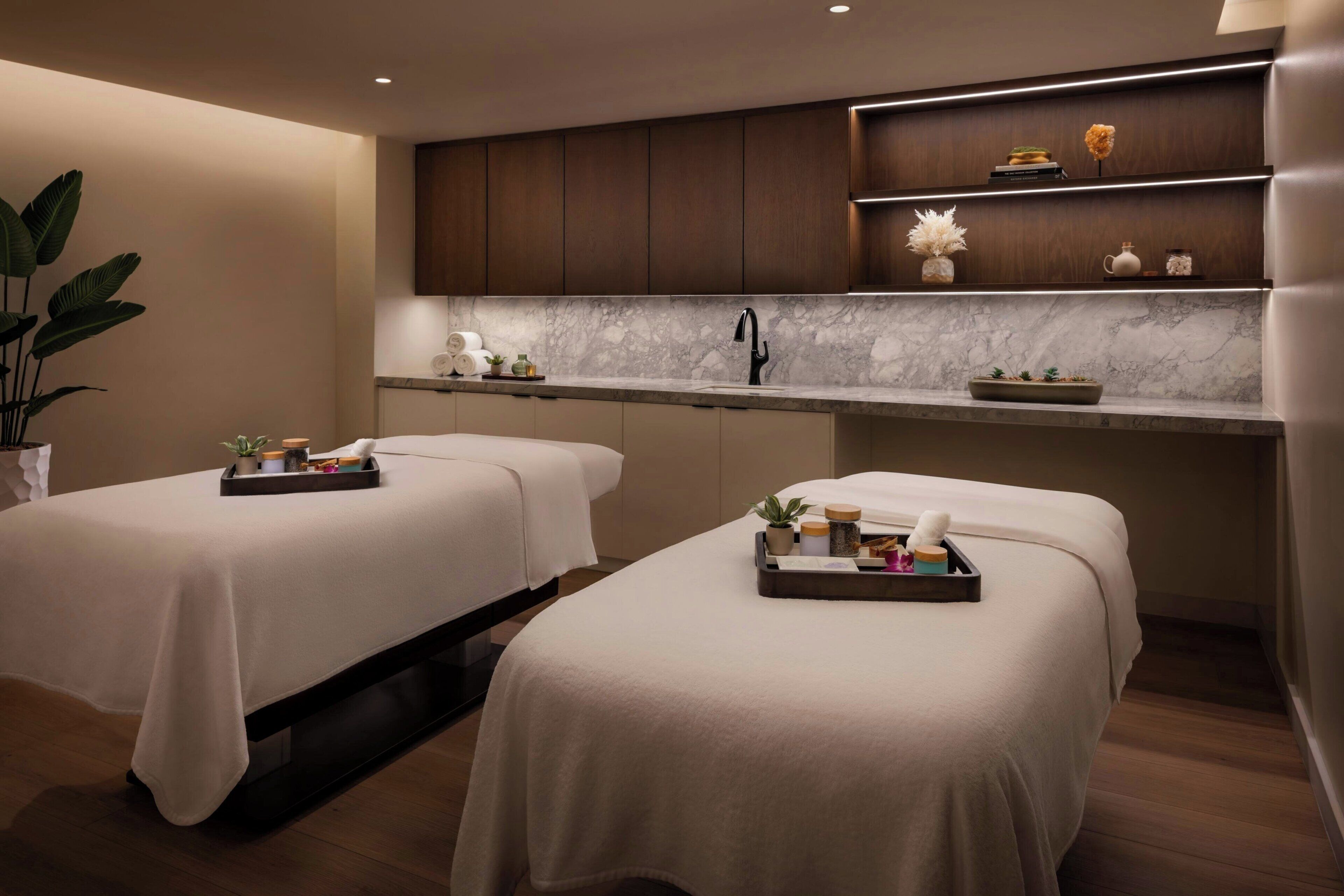 Une salle de spa équipée de deux tables de massage, d’un comptoir en marbre et d’une étagère où sont disposés des objets décoratifs.
