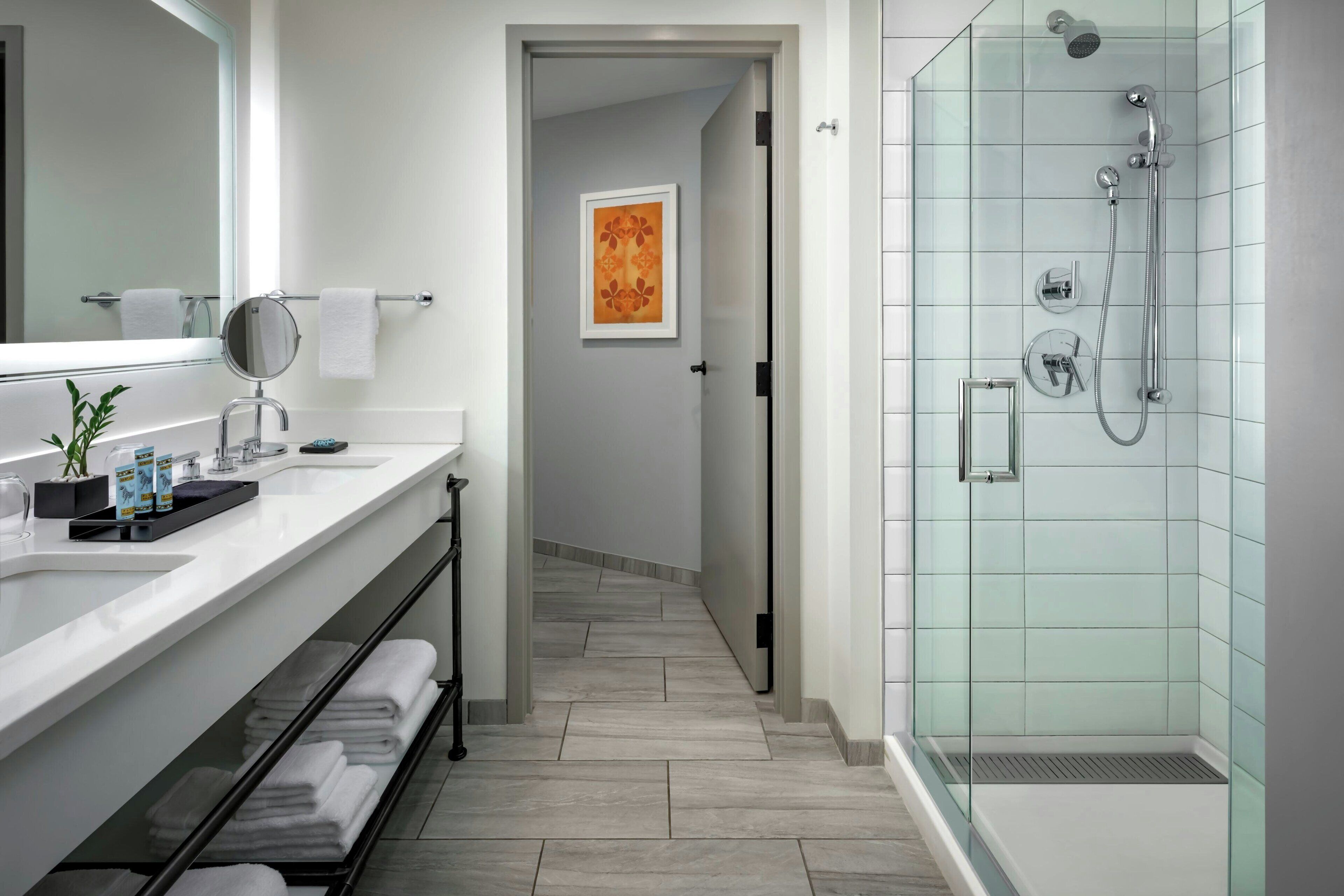 A modern bathroom with a glass-enclosed shower, a large mirror, and a white vanity with a plant.