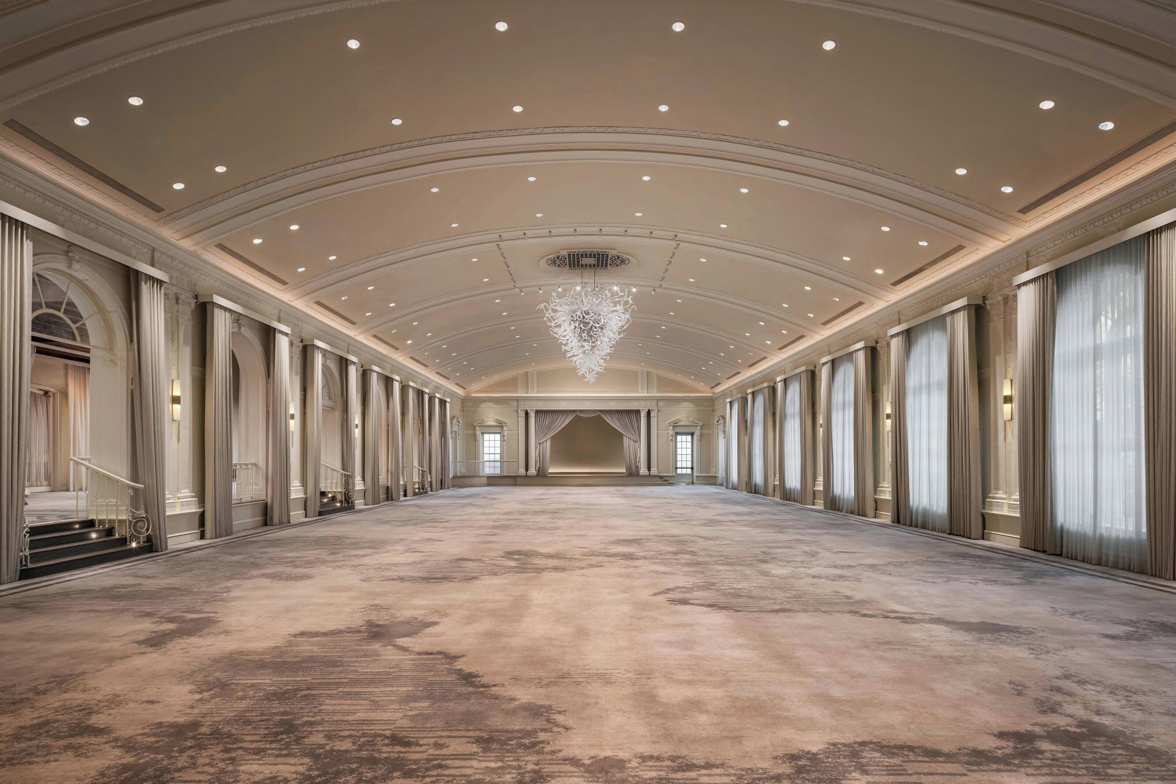 A spacious hall with a high ceiling, recessed lighting, and a central chandelier.