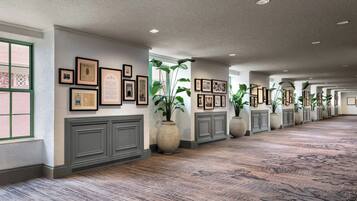 A long hallway with framed pictures on the walls, large potted plants, and a patterned carpet.