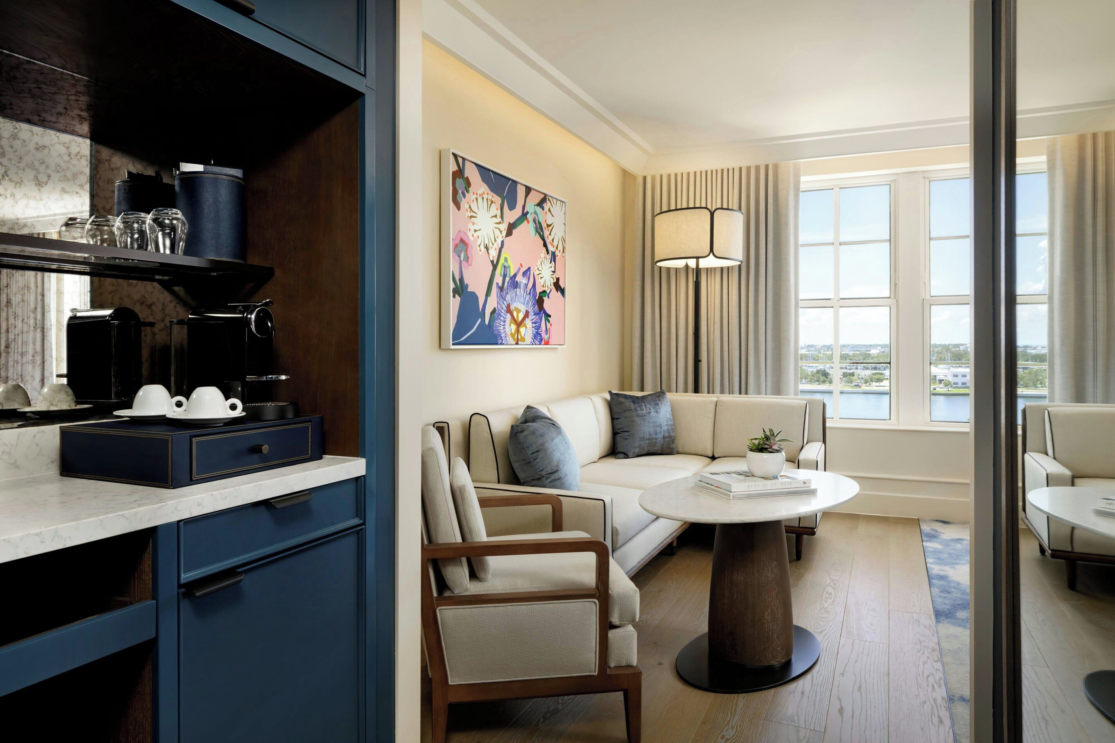 Une chambre d’hôtel moderne dotée d’un coin cuisine, d’un salon avec un canapé et des fauteuils, d’une table à manger et d’une grande fenêtre offrant une vue panoramique.