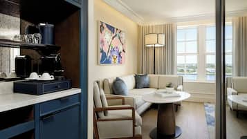 Une chambre d’hôtel moderne dotée d’un coin cuisine, d’un salon avec un canapé et des fauteuils, d’une table à manger et d’une grande fenêtre offrant une vue panoramique.