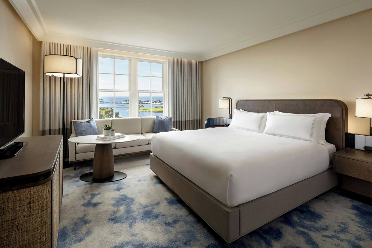 Ein Hotelzimmer mit einem großen Bett, einer Couch, einem Schreibtisch und Meerblick.