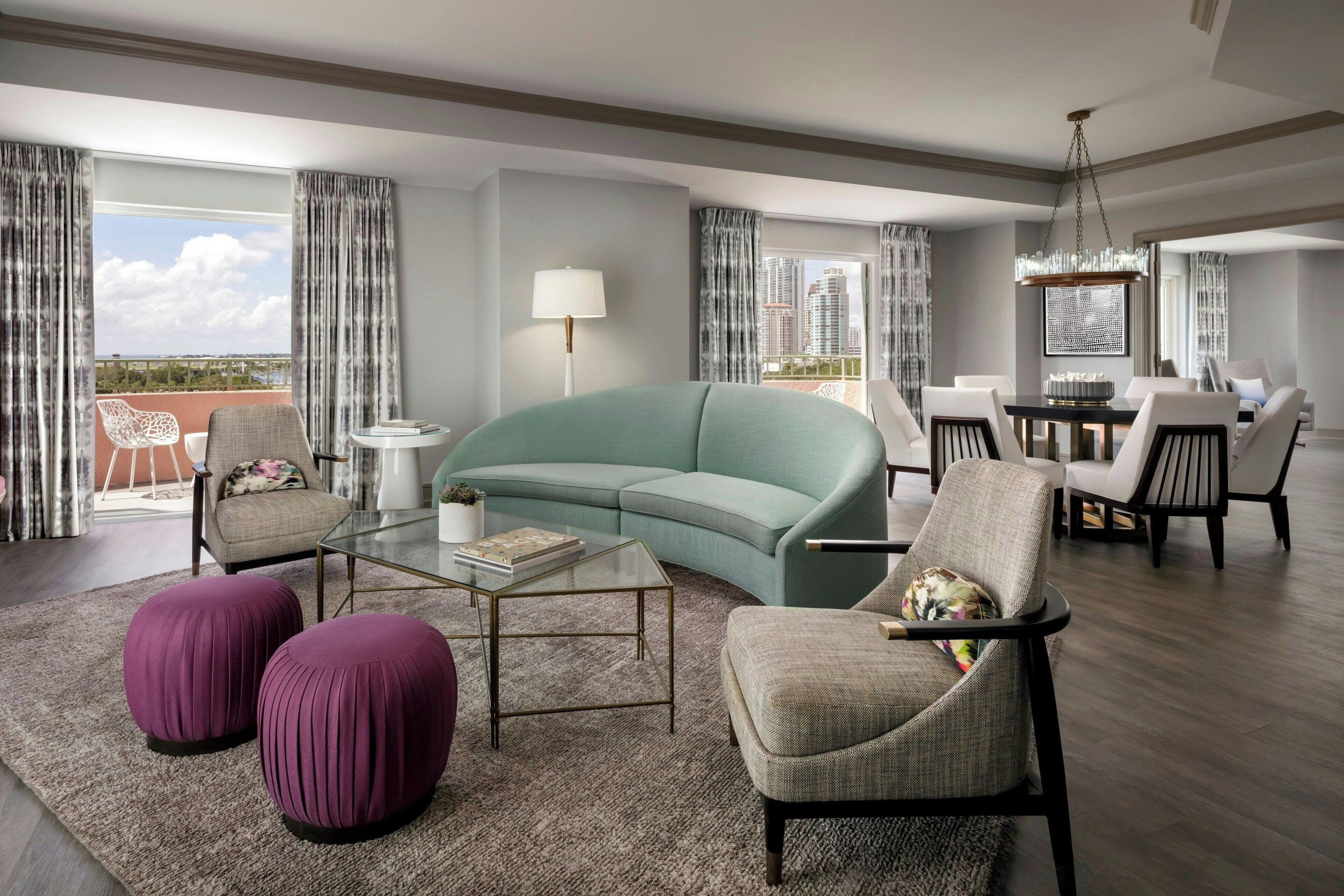 A modern living room with a teal sofa, purple ottomans, and a glass coffee table.