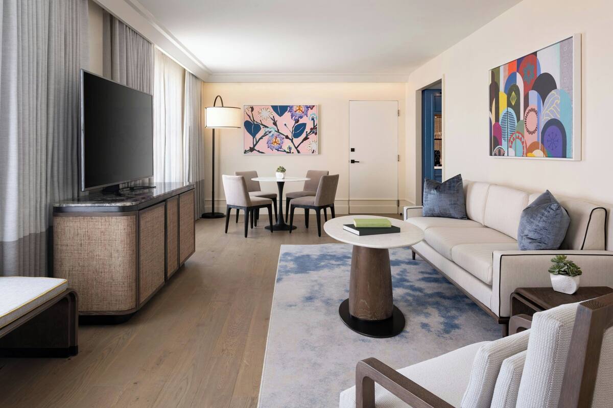 Ein modernes Wohnzimmer mit Flachbildfernseher, Essbereich mit Tisch und Stühlen, einer Couch mit Kissen und einem großen abstrakten Gemälde an der Wand.