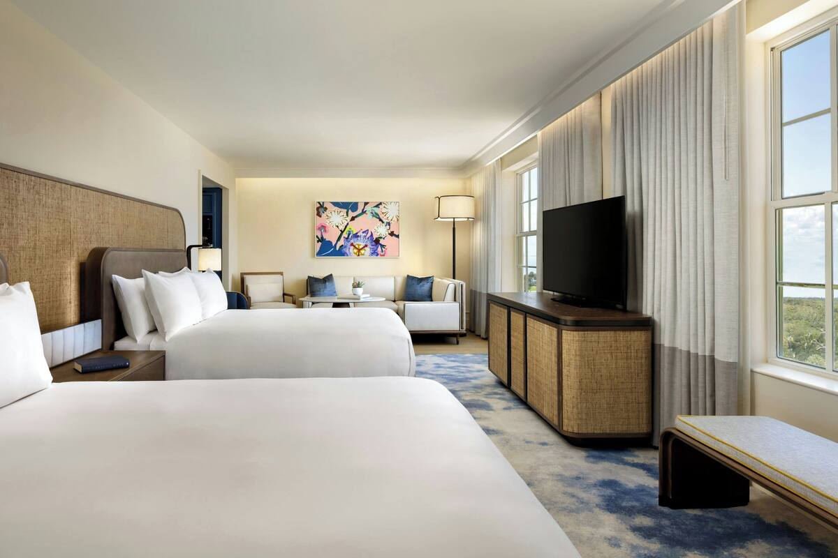 Ein Hotelzimmer mit zwei Betten, einem Fernseher, einem Schreibtisch und einem Fenster mit Vorhängen.