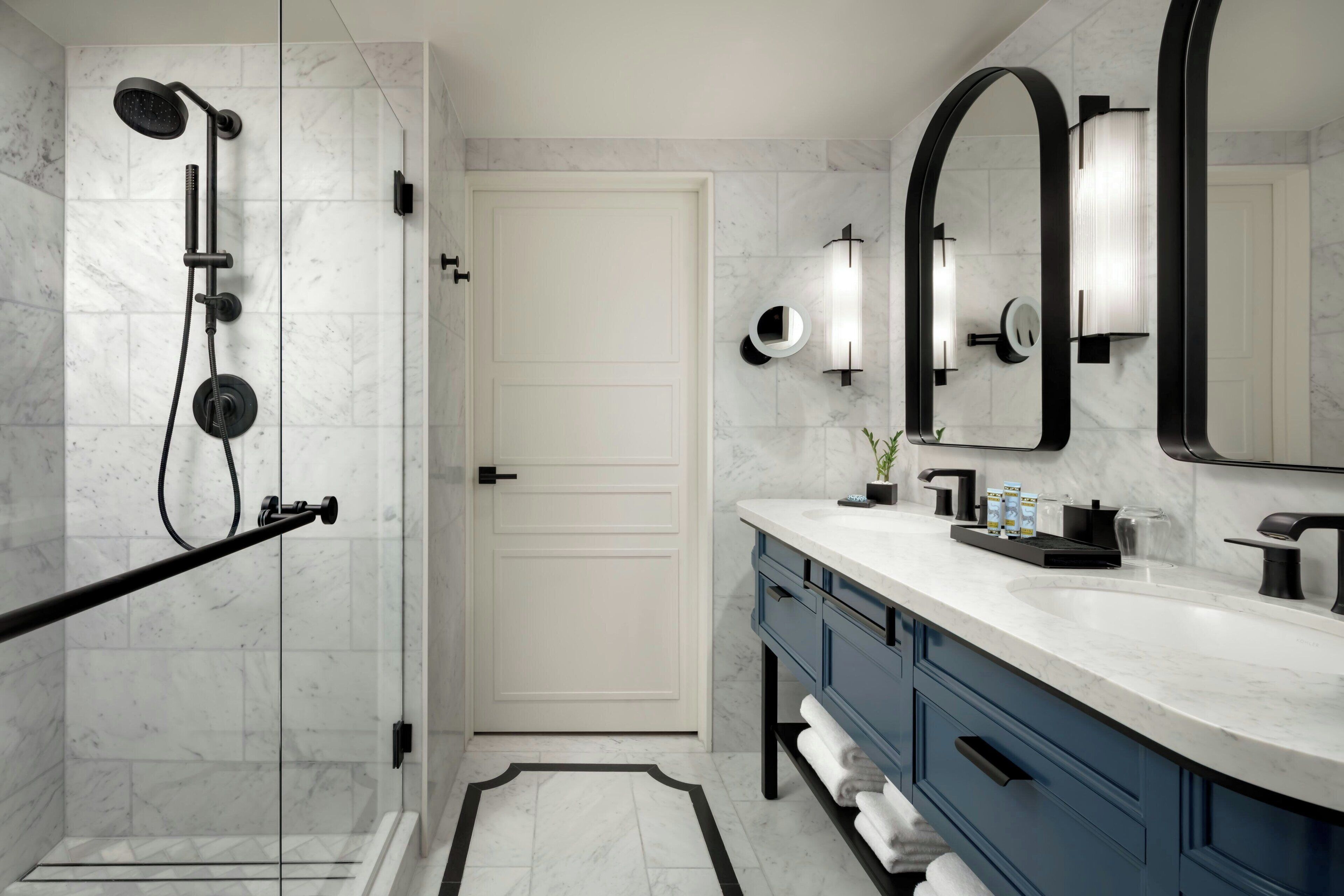 A modern bathroom with a walk-in shower, a large mirror, and a vanity with a marble countertop.