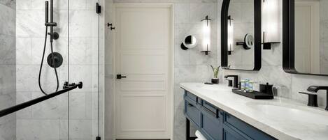 A modern bathroom with a walk-in shower, a large mirror, and a vanity with a marble countertop.