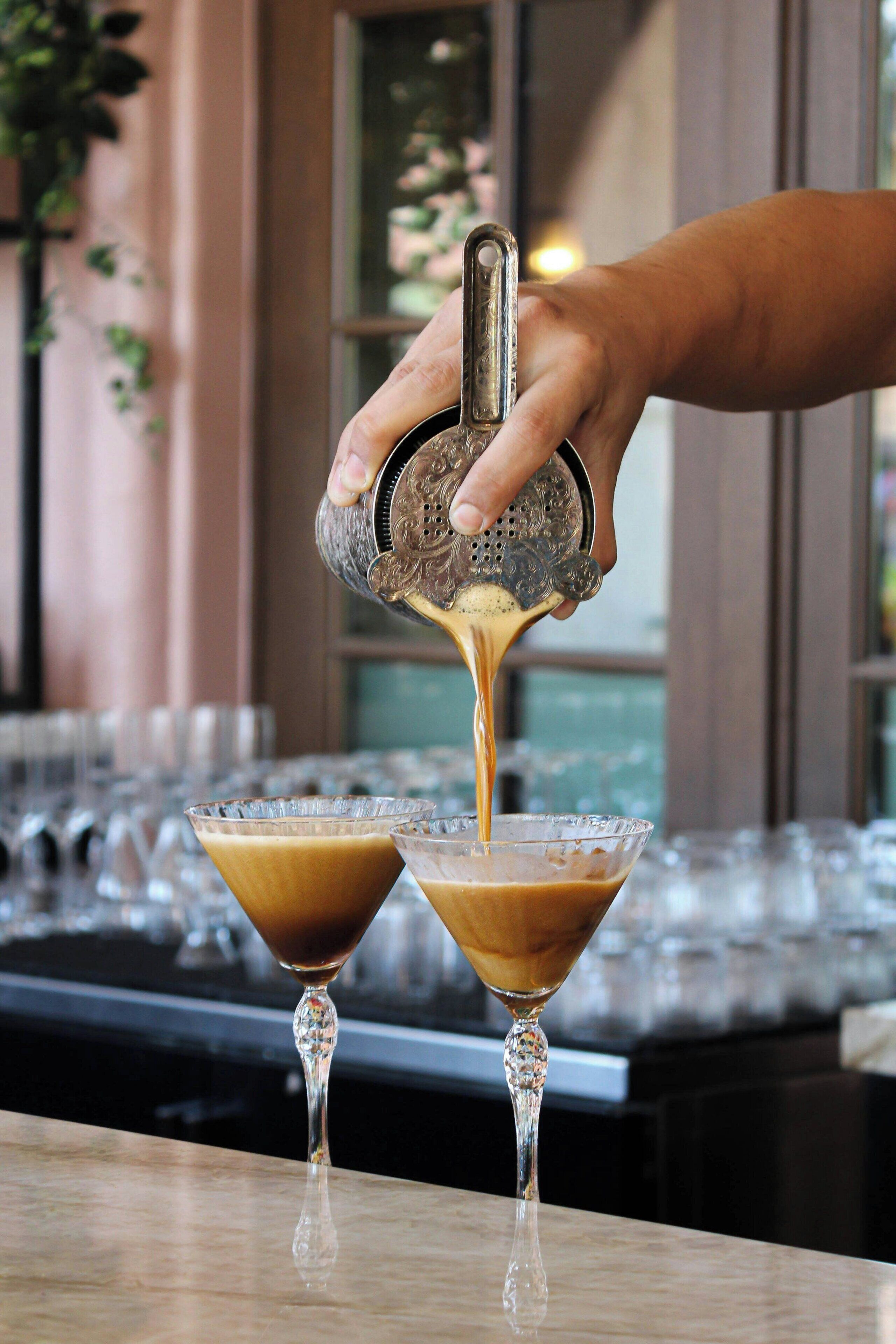 A hand pouring a drink into a martini glass.