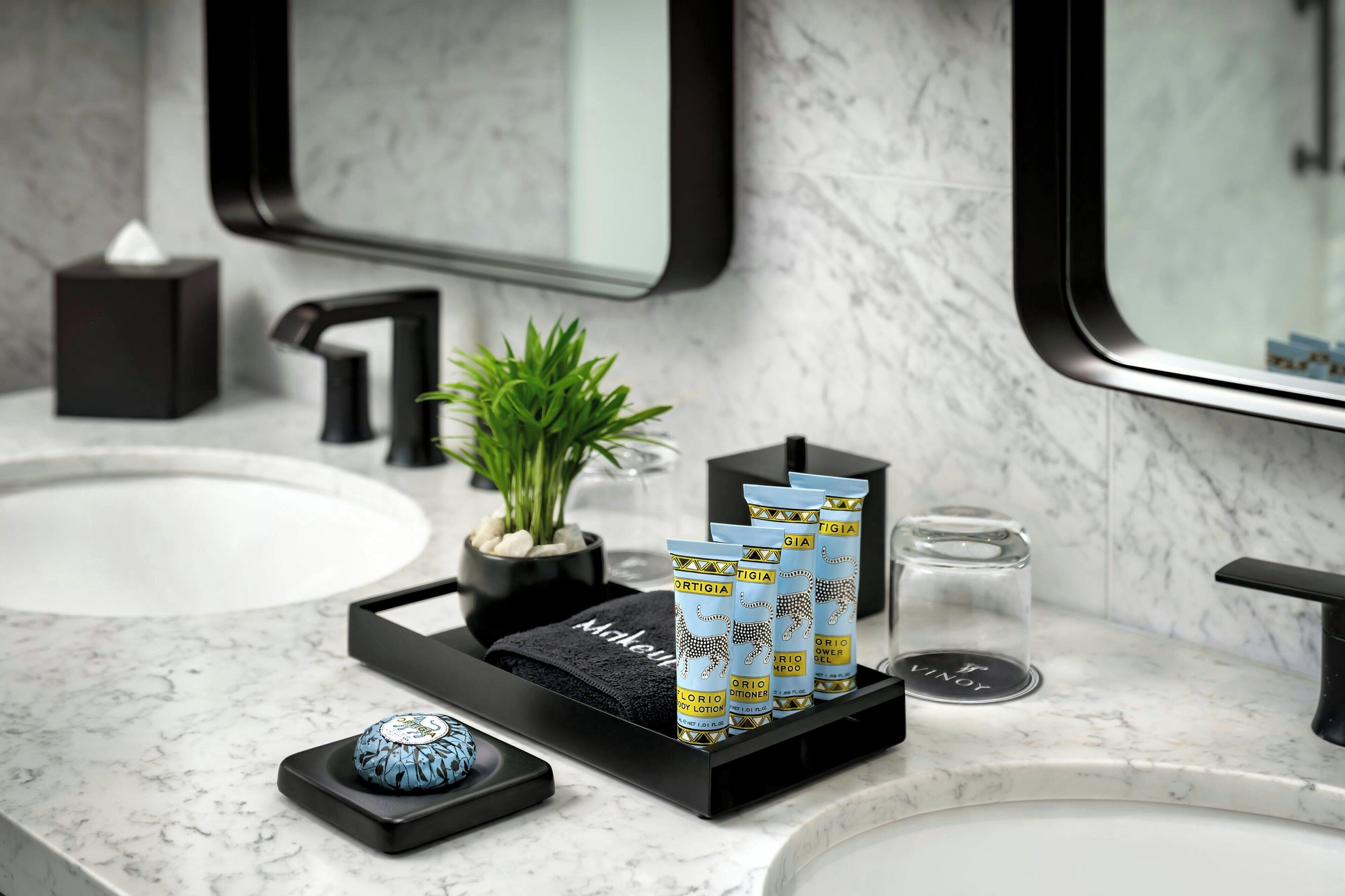 Een badkamer met een marmeren aanrecht, een zwarte dienblad met toiletartikelen, een kleine potplant en een spiegel.