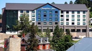 Un hotel Hampton Inn con diseño moderno, que combina fachadas de vidrio y piedra, varios pisos y una señalización destacada.