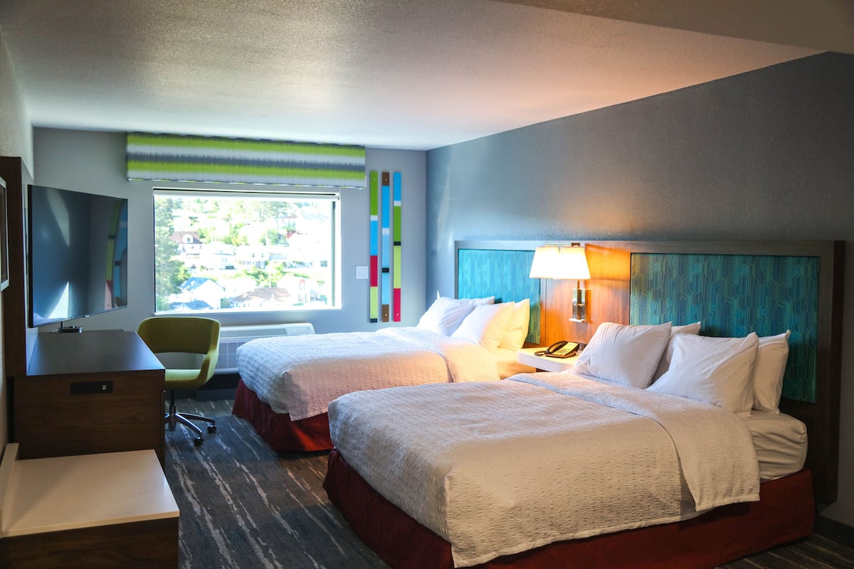 A hotel room with two beds, a desk, a chair, and a TV.