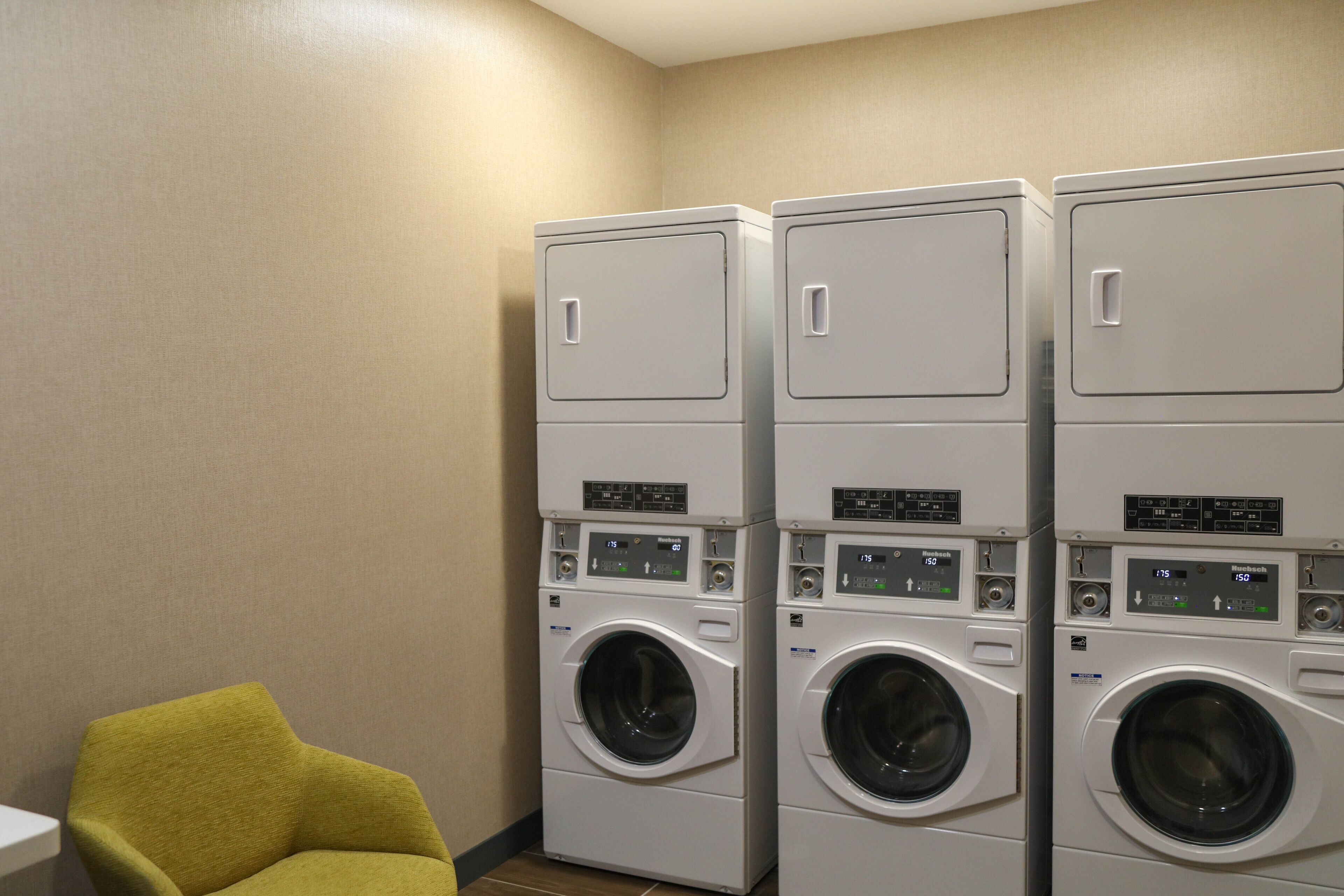 A laundry room with three stacked washing machines and a single chair.