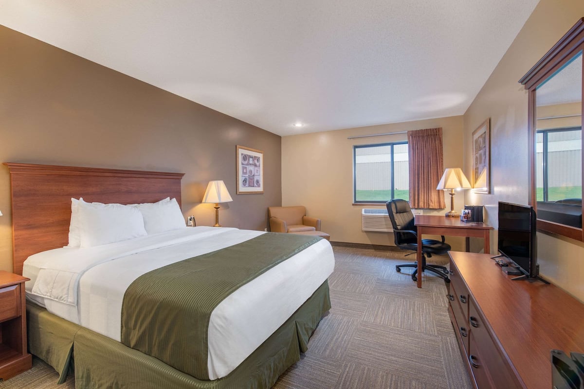 A hotel room with a large bed, a desk with a computer, a chair, and a TV.