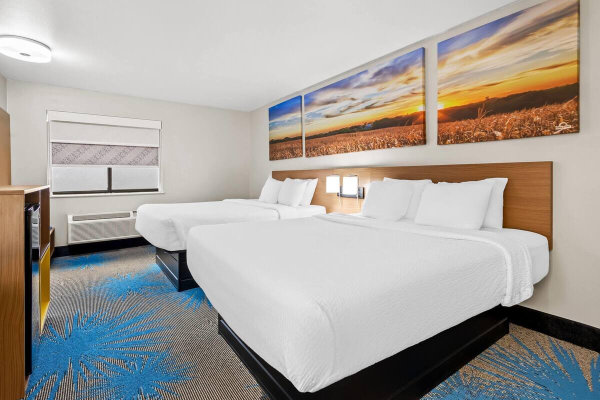 A hotel room with two beds, a large window, and a view of a sunset.