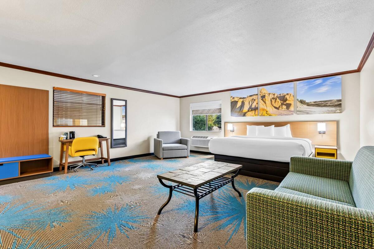 A hotel room with a large bed, a desk, a chair, a sofa, and a view of a rocky landscape through the window.