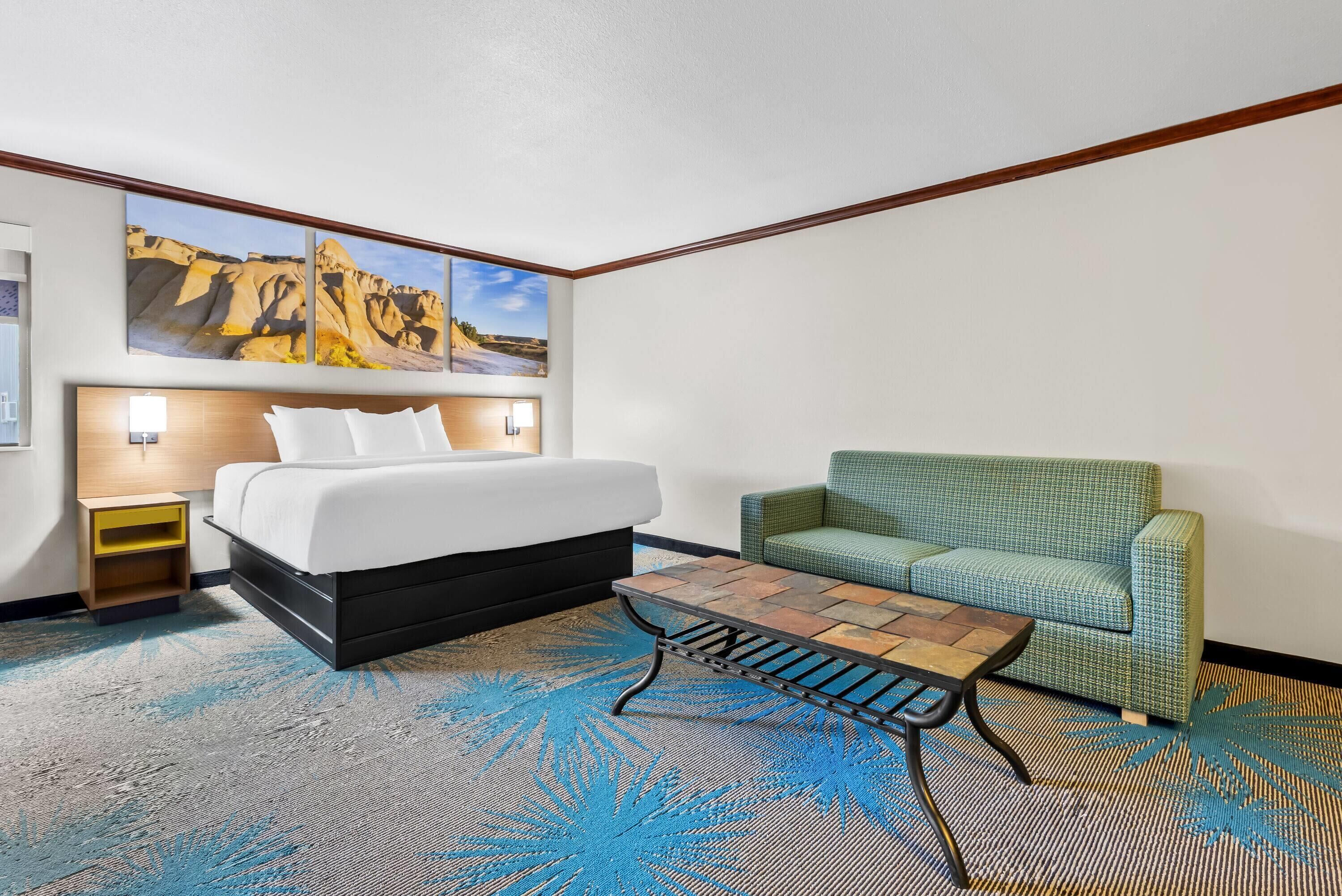 A hotel room with a bed, a green sofa, a coffee table, and a painting of a landscape on the wall.