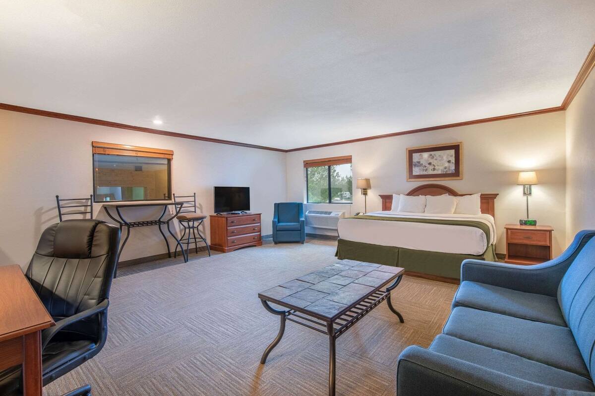 A hotel room with a bed, desk, chair, TV, and a small table.