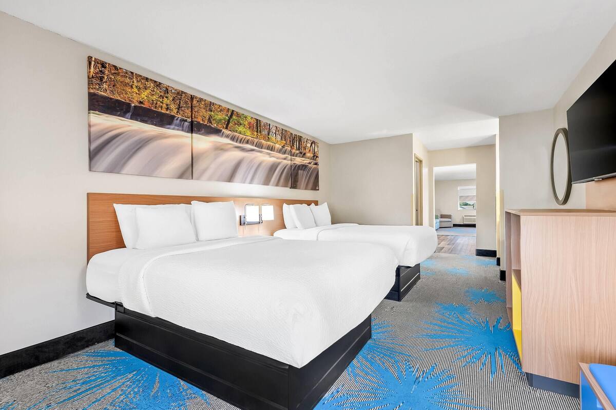 A hotel room with two beds, a large wall mural, a flat-screen TV, and a desk.