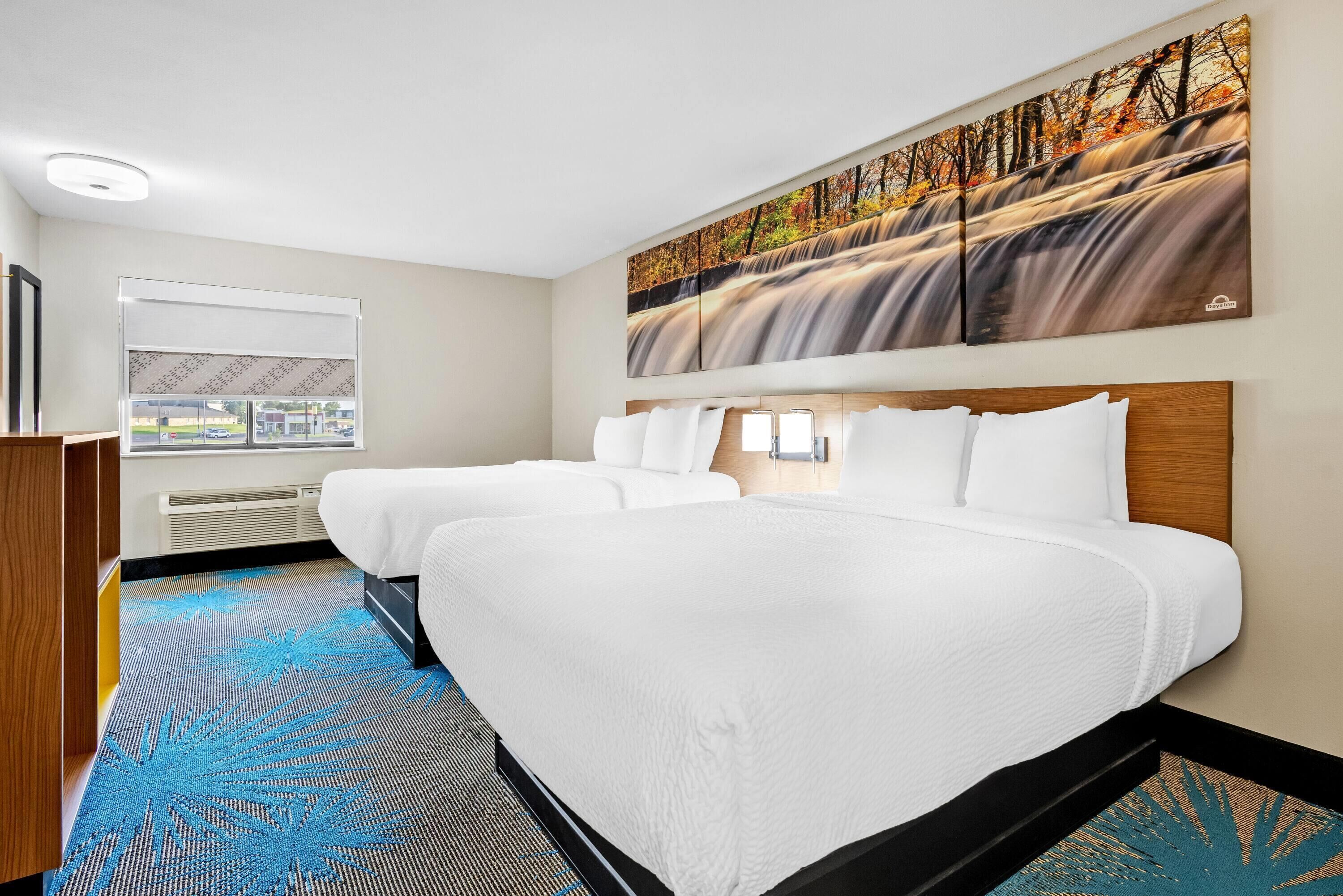 A hotel room with a large bed, a window with a view, and a painting of a waterfall.