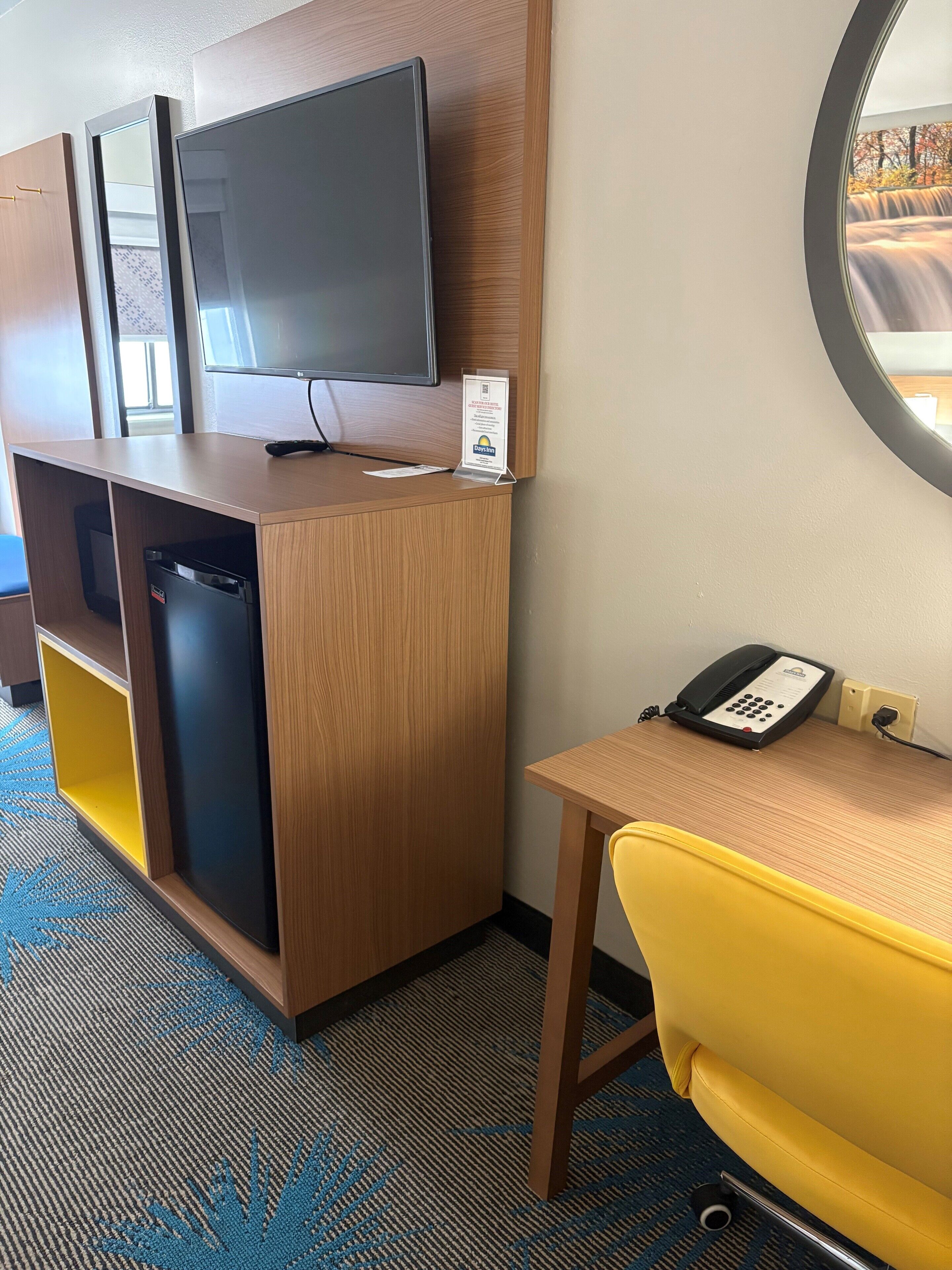 Habitación de hotel con un escritorio de madera, una silla amarilla, televisión, minibar y teléfono.