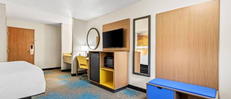 A hotel room with a bed, a desk, a television, a mirror, and a wardrobe.