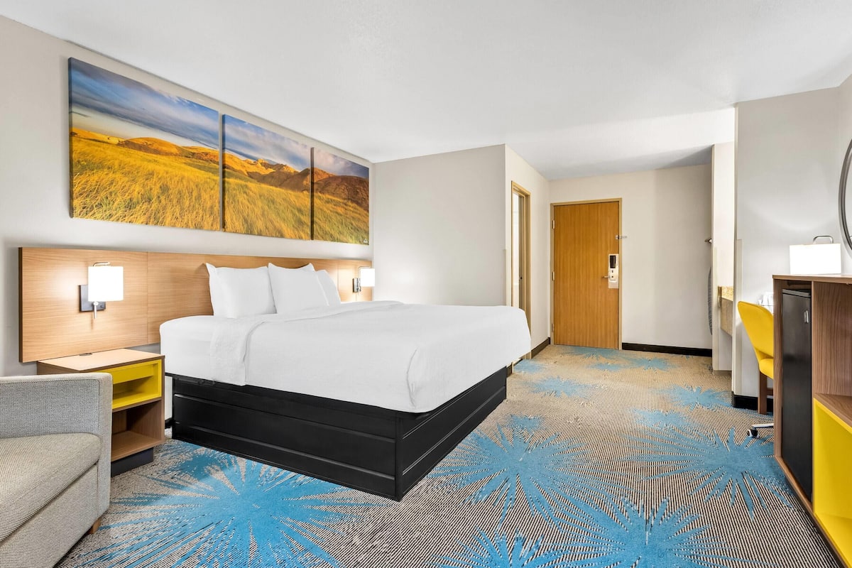 A hotel room with a large bed, a desk, a chair, a wardrobe, and a painting on the wall.